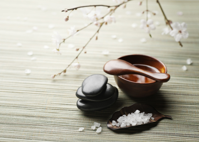 A table with a cup of massage oil a plate of salt and a massage stone
